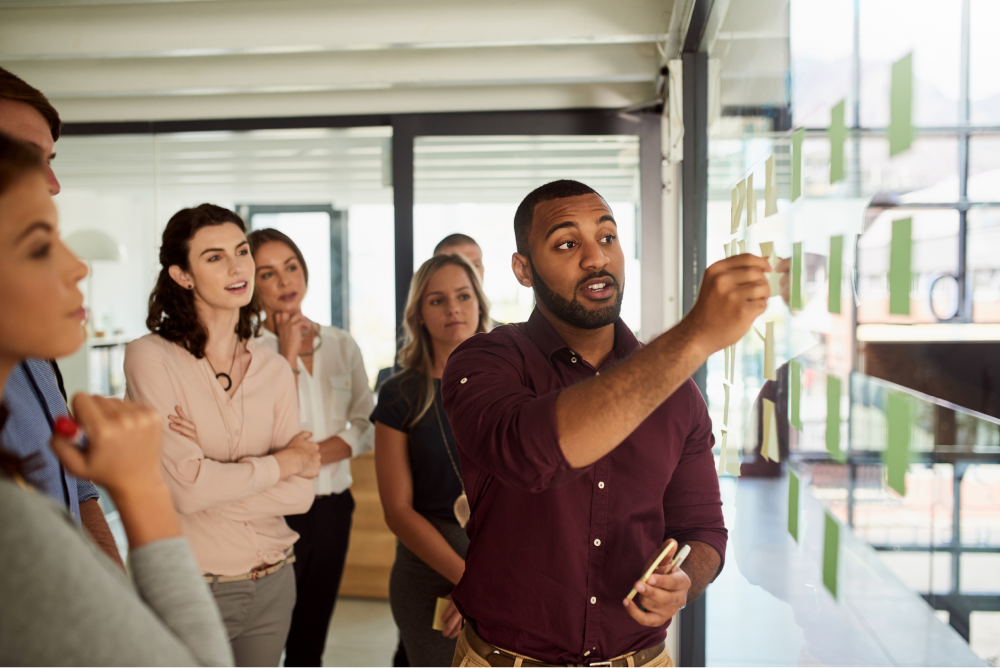 An office worker leads collaboration with a team using sticky notes on a glass wall